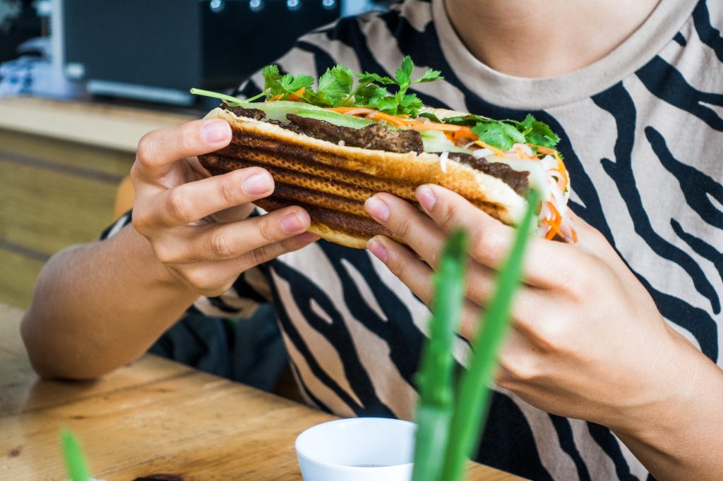 Girl holding Vietnamese baguette Banh Mi with fresh vegetables and grilled pork