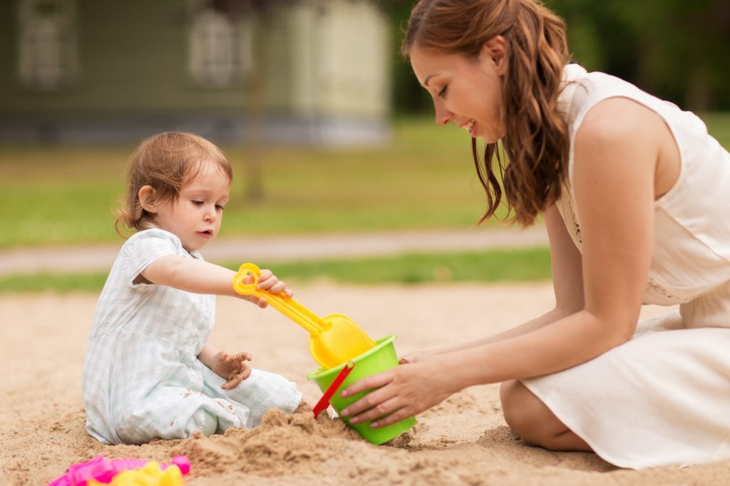 happy mother with baby girl playing in sandbox